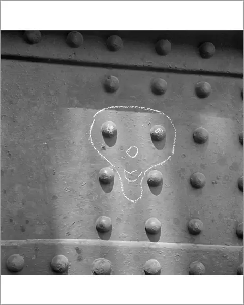 Face drawn in chalk around metal rivets, London Docks a064944